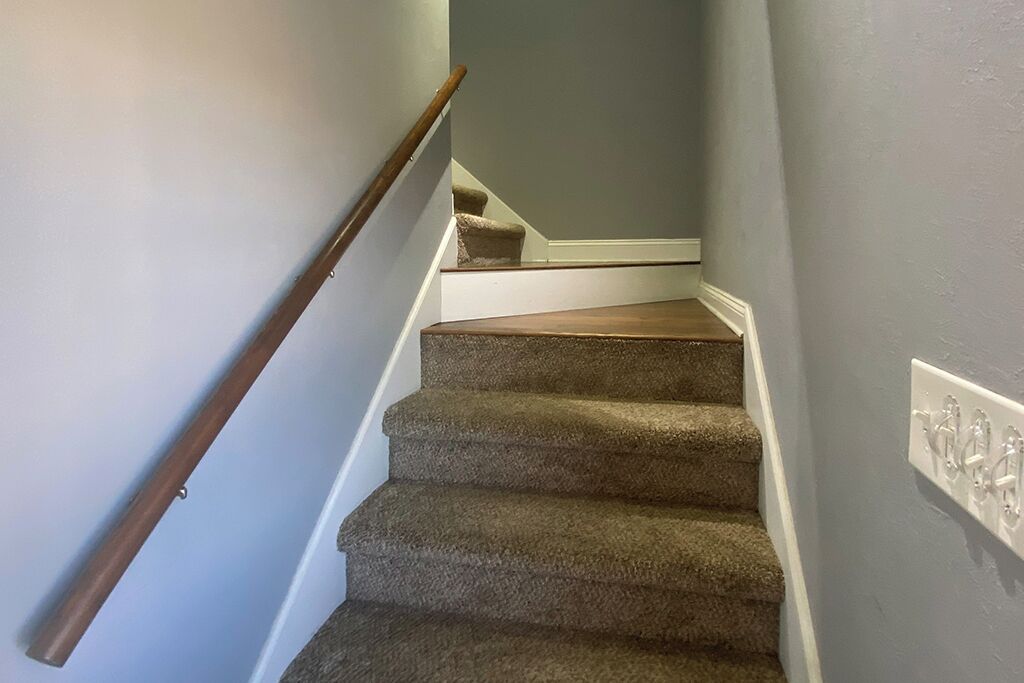 Un escalier recouvert de moquette, avec une rampe en bois et un mur bleu clair.