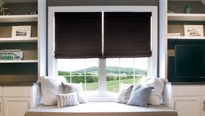 A bay window with a view of green hills, white cabinetry, and a television on the right.