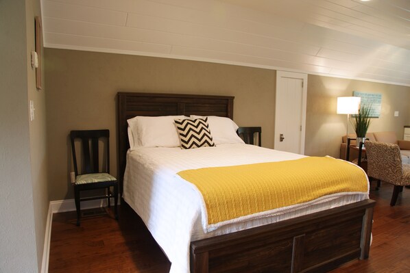 A neatly made bed with a wooden headboard, a yellow throw blanket, and a chevron pillow. There is a chair with a patterned cushion next to the bed. - Beautiful Modern Loft In Wine Country! (Ste. Genevieve)