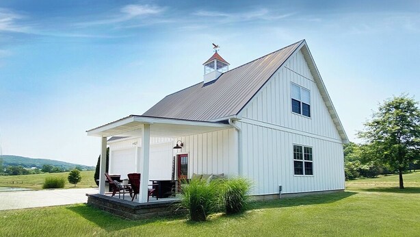 A white two-story house with a covered porch, a chimney, and a small garden area with chairs and a table.