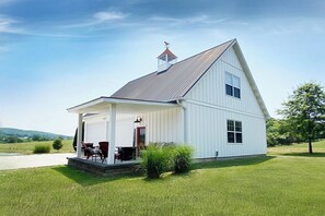 Une maison blanche à deux étages, dotée d’un porche abrité, d’une cheminée et d’un petit jardin avec des chaises et une table.