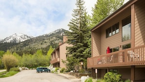 A two-story building with a balcony, a mountain backdrop, and a parked car in front.