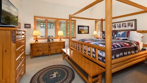 A four-poster bed with a quilt, wooden dresser, bedside lamps, and a framed picture above the bed.