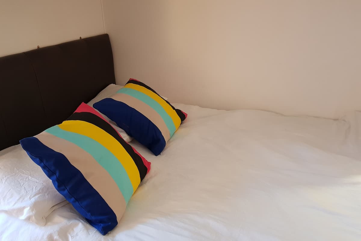 A bed with white sheets and two colorful striped pillows.