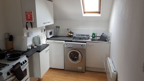 Eine kleine Küche mit Herd, Mikrowelle, Waschmaschine und einem kleinen Fenster.