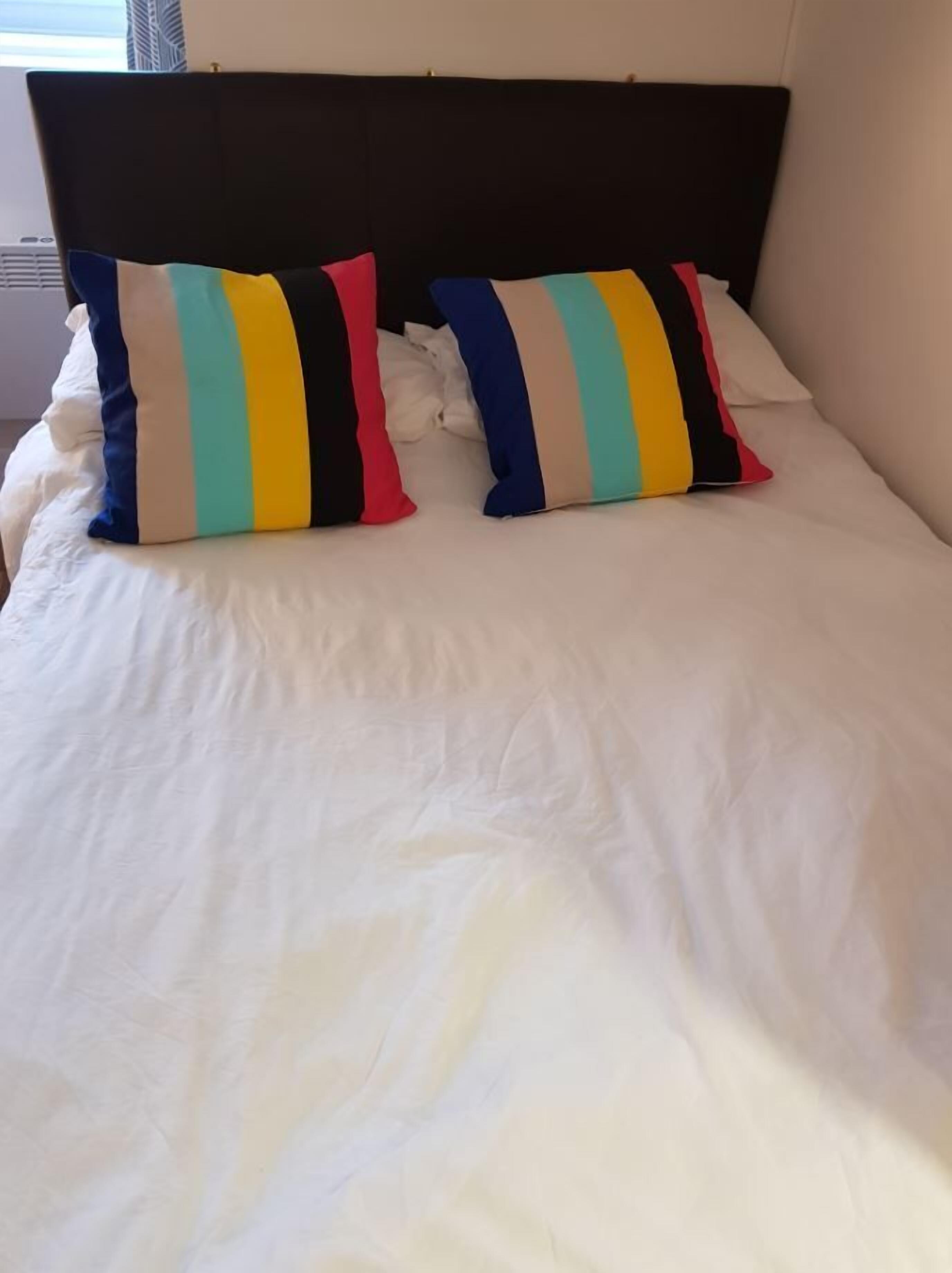Cama com roupa de cama branca e duas almofadas listradas.