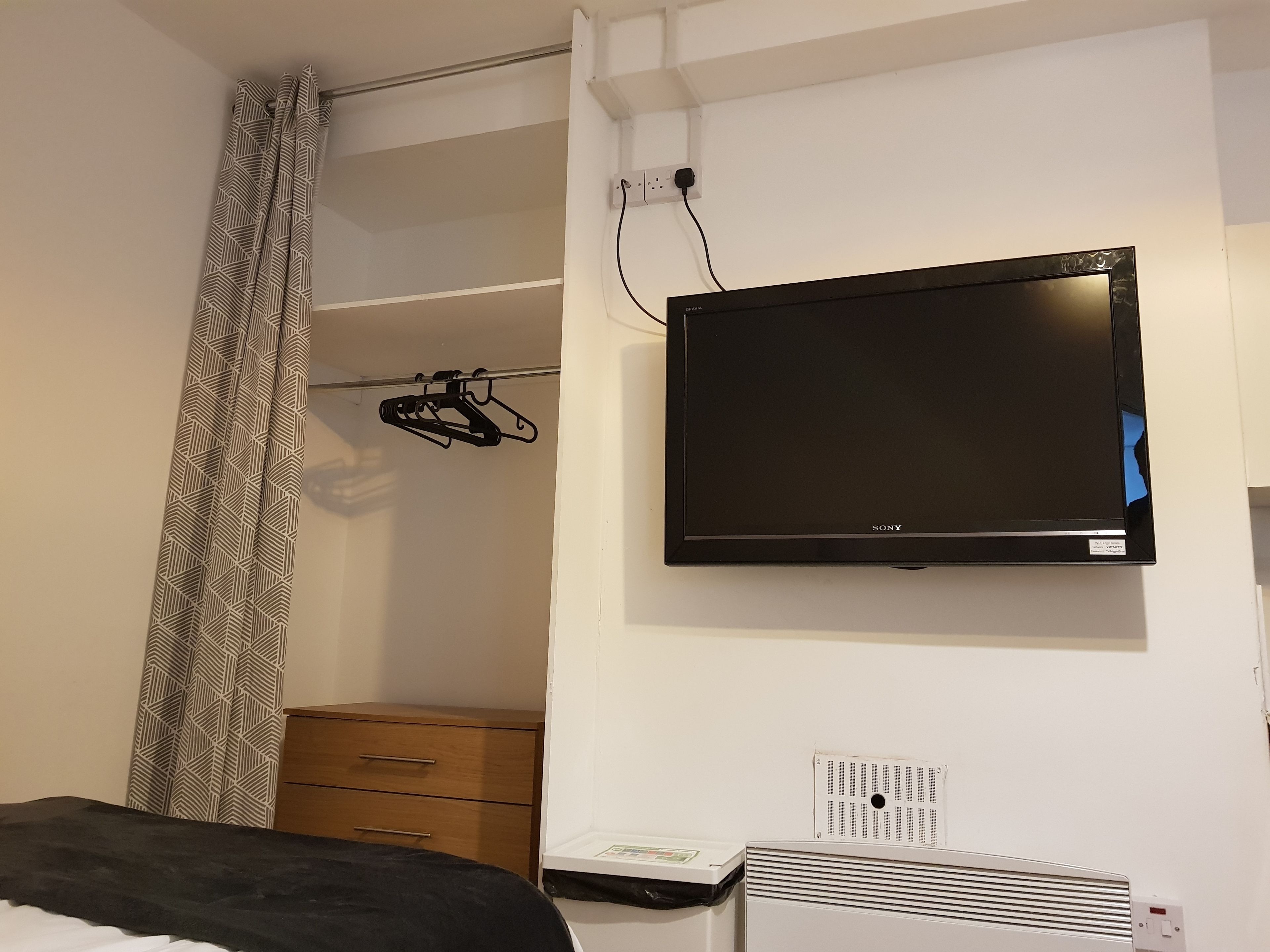 A bedroom with a bed, a wardrobe, a flat-screen TV mounted on the wall, and a heater.