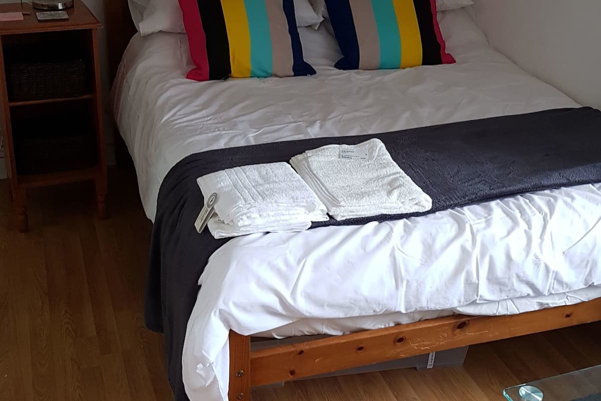 A neatly made bed with a striped pillow, a bedside table with a lamp, and a glass table beside the bed.