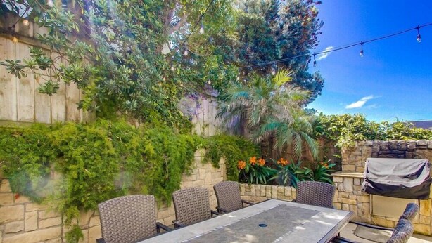 Un patio al aire libre con una mesa y sillas, rodeado de vegetación exuberante y un muro de piedra.