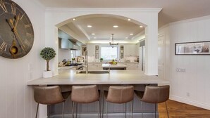 Una cocina moderna con una isla central, taburetes de bar y un reloj de pared grande.
