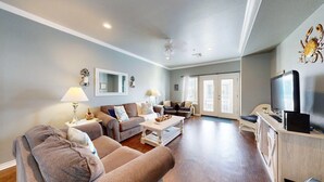 A spacious living room with a sofa set, a coffee table, and a television. - Shared Pool and Hot Tub, Garage, Golf Cart Access, Pet Friendly (Port Aransas)