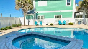 A swimming pool with a hot tub, surrounded by a white fence and a green building in the background. - Shared Pool and Hot Tub, Garage, Golf Cart Access, Pet Friendly (Port Aransas)