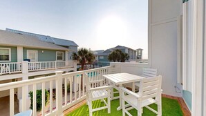 A balcony with a white table and chairs, surrounded by a white railing. - Shared Pool and Hot Tub, Garage, Golf Cart Access, Pet Friendly (Port Aransas)