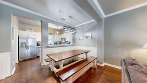 A modern kitchen with white cabinetry, a stainless steel refrigerator, and a wooden dining table with benches. - Shared Pool and Hot Tub, Garage, Golf Cart Access, Pet Friendly (Port Aransas)