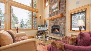 A cozy living room with a stone fireplace, large windows, and comfortable seating.