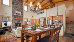 A spacious living area with a fireplace, dining table set for four, and a kitchen with wooden cabinets and modern appliances.