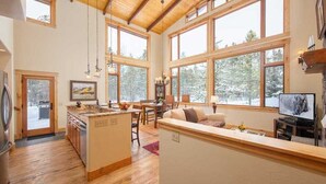 A spacious kitchen with wooden flooring, large windows, and a dining area with a view of snowy trees.