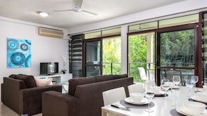A modern living room with a sofa set, a dining table set for six, and large windows offering a view of greenery. - Tranquility Chill at Palm Cove (Palm Cove)