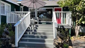 A house with a front porch, a staircase leading to the entrance, and a patio area with a table and chairs. - Under the Oaks Santa Barbara (Santa Barbara)