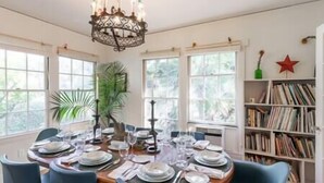 A dining room with a round table set for six, surrounded by chairs, a chandelier, and a bookshelf with books. - Under the Oaks Santa Barbara (Santa Barbara)
