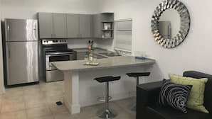 A modern kitchen with grey cabinets, a stainless steel refrigerator, an oven, and a built-in island with bar stools. - Cozy 4 Bdrm 2Bath Home close to Design District, Wynwood #ArtBasel #MiamiBeach (Miami)