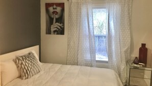 A bedroom with a bed, a bedside table, a wall-mounted picture, and a window with curtains. - Cozy 4 Bdrm 2Bath Home close to Design District, Wynwood #ArtBasel #MiamiBeach (Miami)