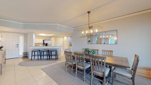 Un comedor amplio con una gran mesa de madera y sillas, una cocina al fondo y una lámpara moderna.