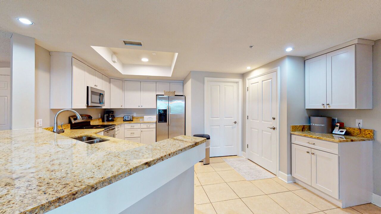 Una cocina moderna con armarios blancos, encimeras de granito, microondas integrado y refrigerador de acero inoxidable.