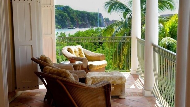 A balcony with wicker furniture, a view of a tropical landscape, and a white door.