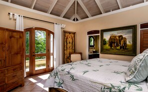 A bedroom with a large bed, a wooden wardrobe, a door with a glass panel, and a painting of elephants. - Reefside Villa: Full AC! Pool! Private sandy beach! (St John)