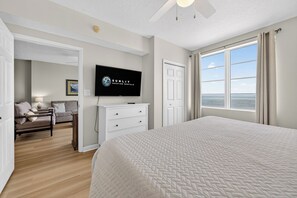 A bedroom with a large bed, a television, a desk, and a view of the ocean.