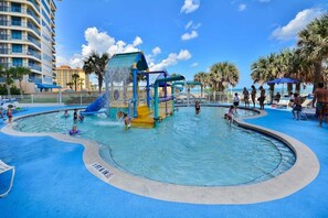 A water park with a play structure, swimming pool, and palm trees.