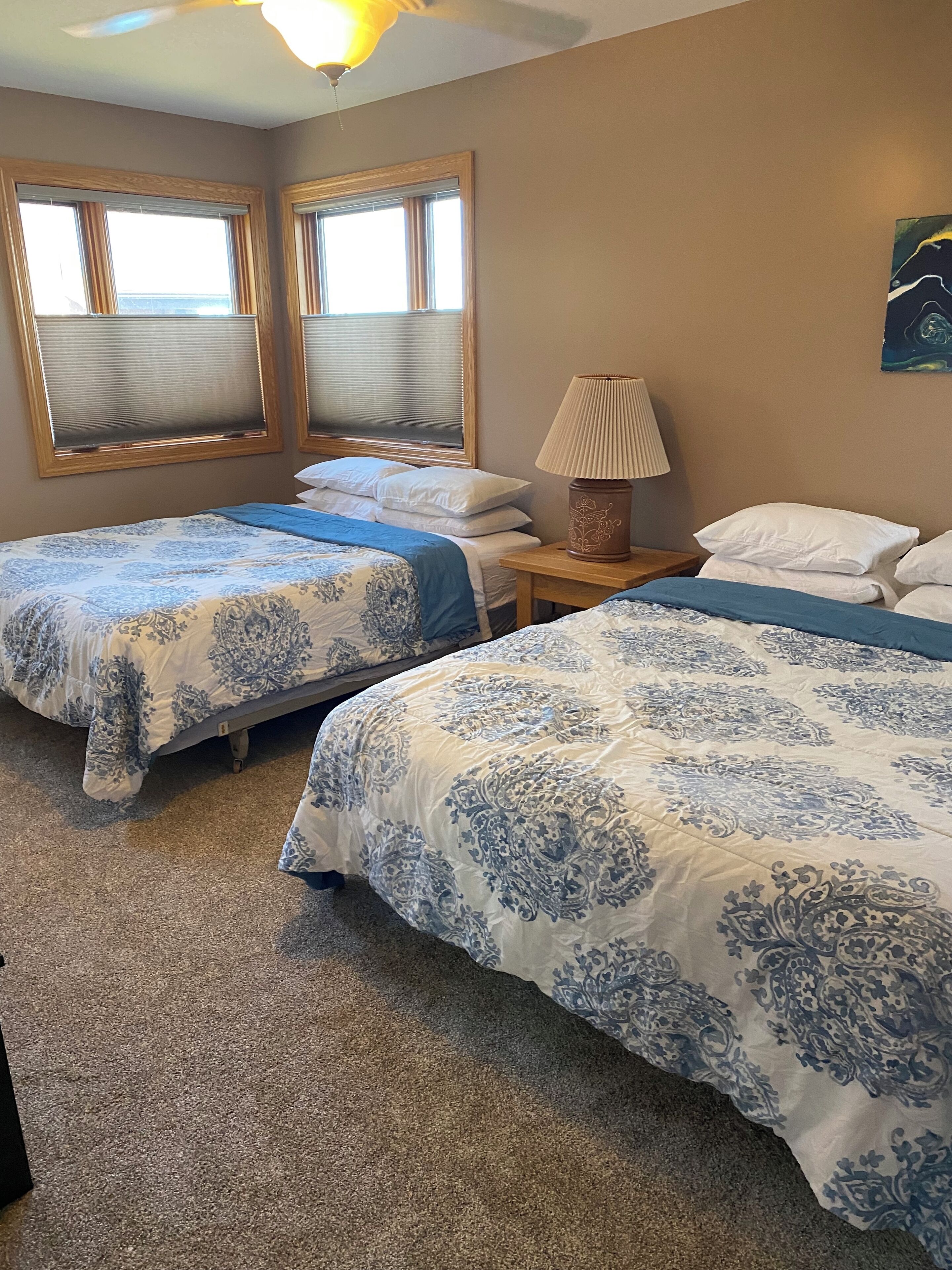 A hotel room with two beds, a nightstand, a lamp, and a painting on the wall.