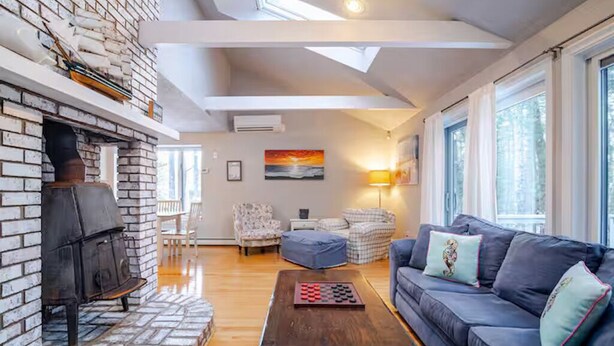 Una sala de estar con chimenea, un sofá, una mesita de centro y vistas al exterior a través de grandes ventanales.