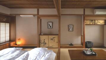 A traditional Japanese room with tatami flooring, a low wooden table with a tray, a bed with white bedding, and a window with vertical blinds.