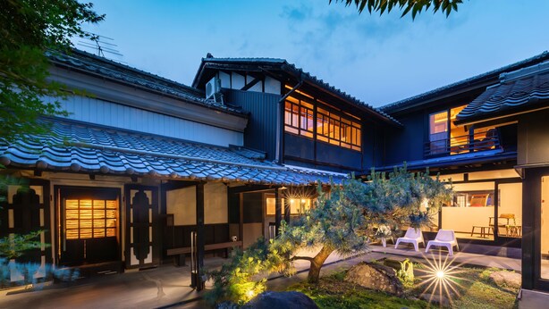 A traditional Japanese-style building with a covered patio area, stone lanterns, and a small tree. - Machiya Hotel Oyado Baison (Mino)