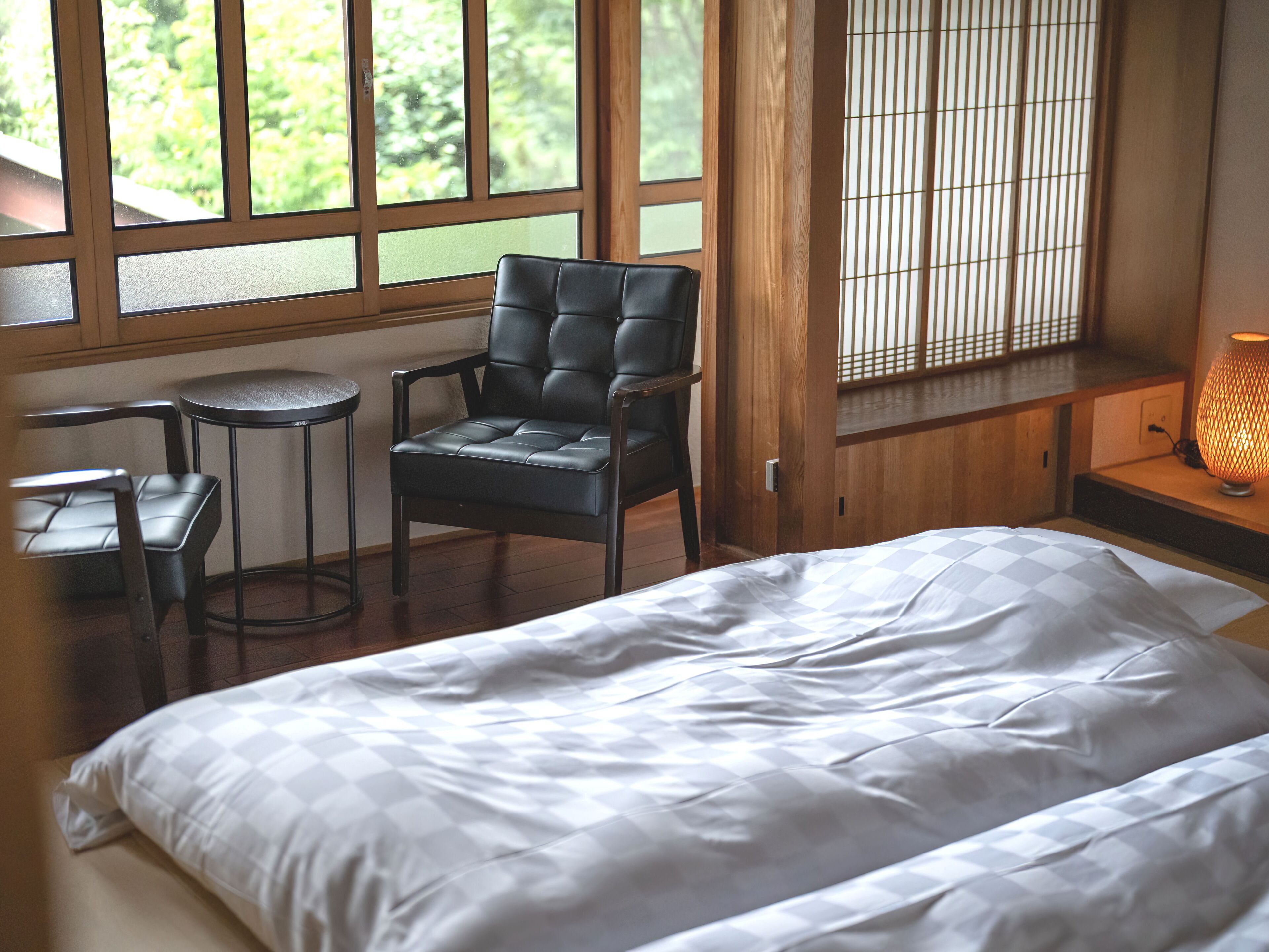 A bedroom with a bed, a chair, a small table, and a window with blinds.