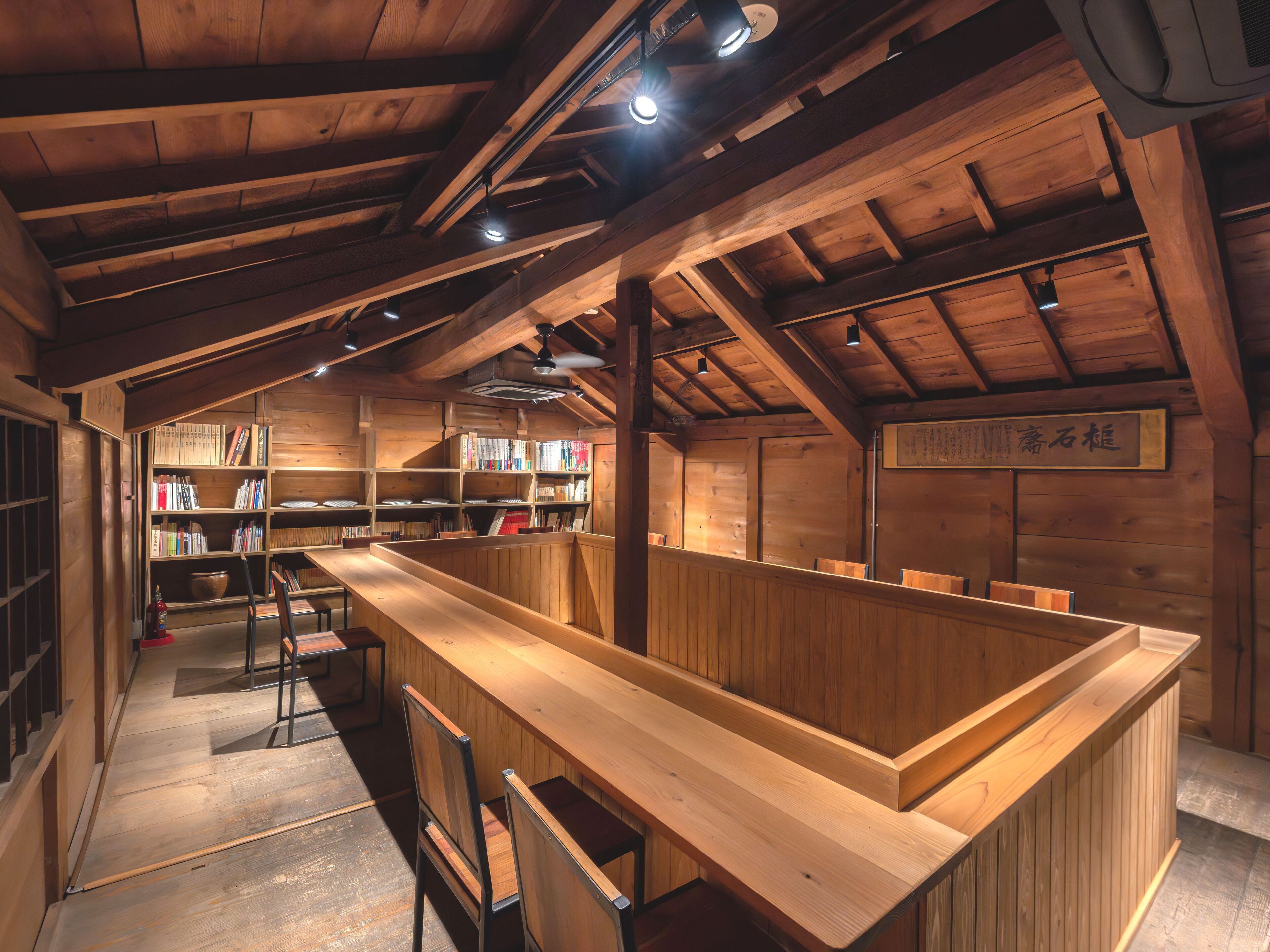 A wooden interior with bookshelves, a long wooden counter, and a sign with Japanese characters.