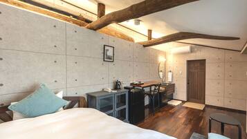 A bedroom with a bed, a desk, and a chair. There is a wooden ceiling beam and a wall-mounted light fixture.