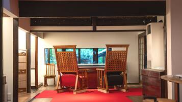 A room with a red carpet, wooden chairs, a table, and a large window with a view of greenery.