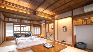 A traditional Japanese-style room with tatami flooring, a wooden table, a bed, and a sliding door. - Machiya Hotel Oyado Baison (Mino)