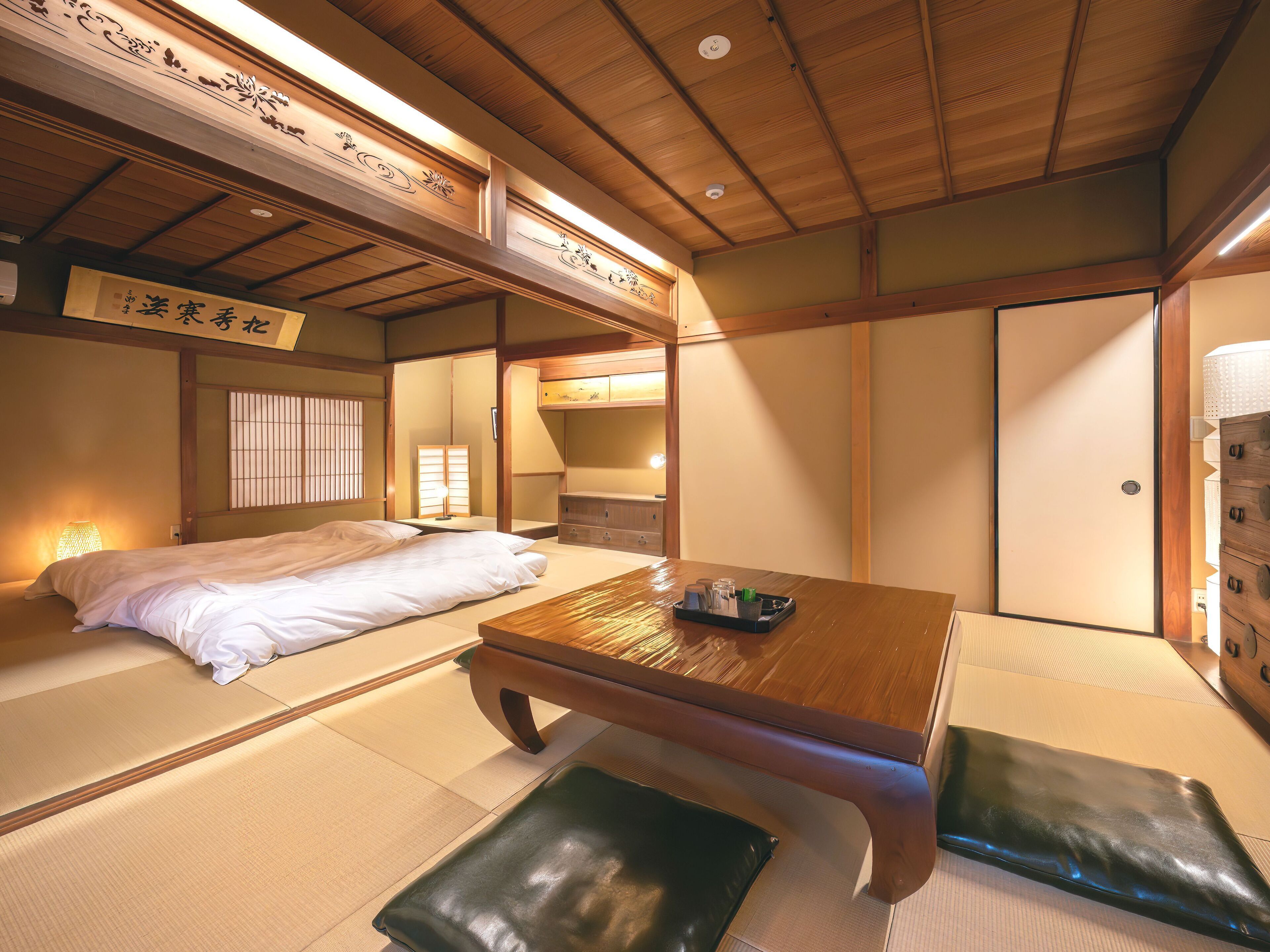 A traditional Japanese room with tatami flooring, a low wooden table, a bed with white bedding, and sliding doors.