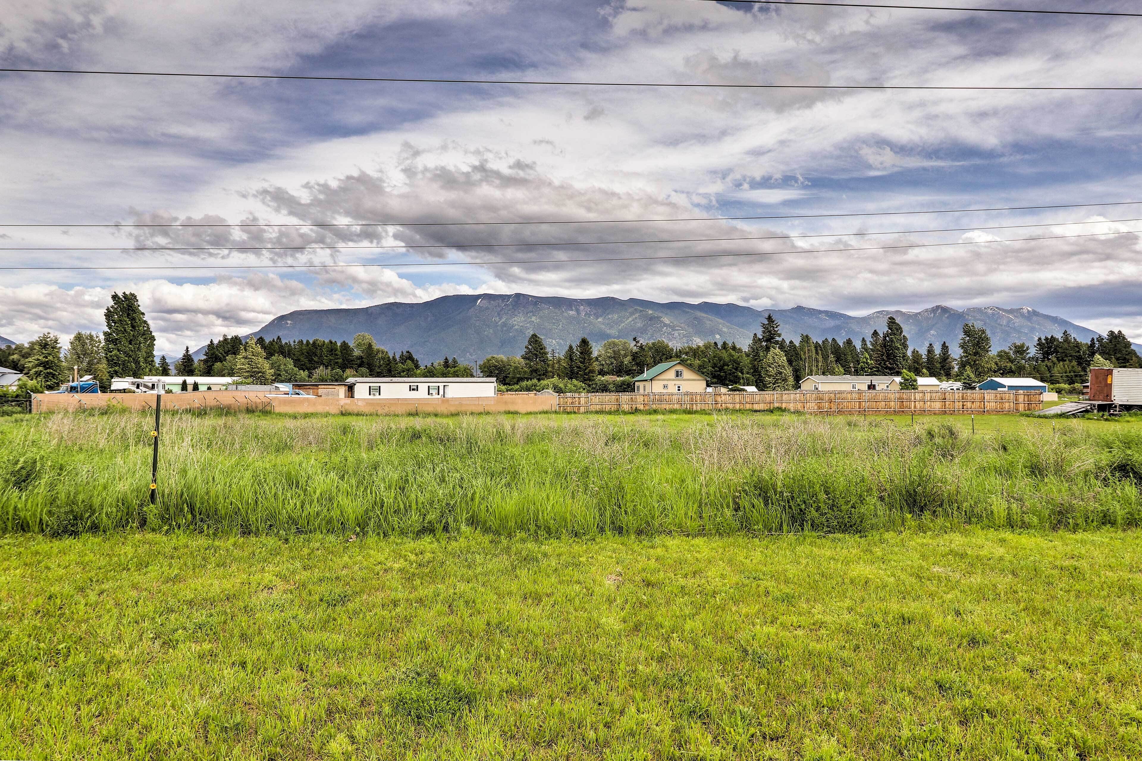 A rural landscape with a field, a few buildings, and mountains in the background.