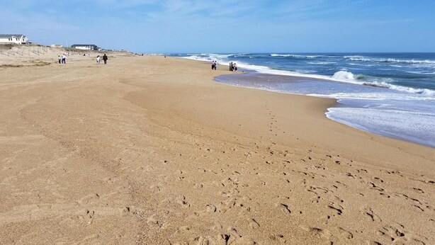 Une vaste plage de sable, parsemée d’empreintes, avec quelques personnes et les vagues de l’océan.