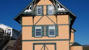 Un bâtiment à deux étages avec une grande porte de garage, un escalier sur le côté gauche et des tables de pique-nique à l’avant.