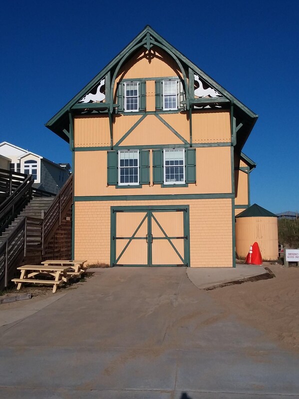 A two-story building with a large garage door, a staircase on the left, and picnic tables in front.