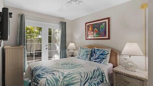 A bedroom with a bed, a nightstand, a lamp, a ceiling fan, a window with curtains, and a door leading to an outdoor area. - ABOUT TIME at The Truman Annex in Key West (Key West)