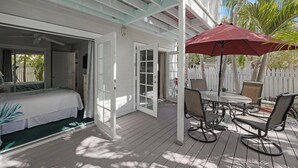 A covered outdoor area with a bed, a dining table with chairs, and a red umbrella. - ABOUT TIME at The Truman Annex in Key West (Key West)