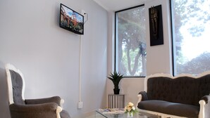 Un salon comprenant un canapé, un fauteuil, une table basse en verre et un téléviseur fixé au mur.