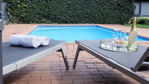 Un espace aménagé au bord de la piscine, avec des chaises longues, une bouteille de champagne et un plateau contenant des verres et des amuse-gueules.